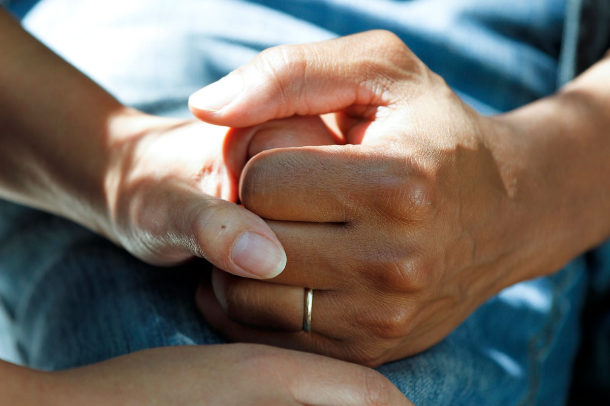 Manos de una cuidadora sosteniendo la mano de una persona mayor